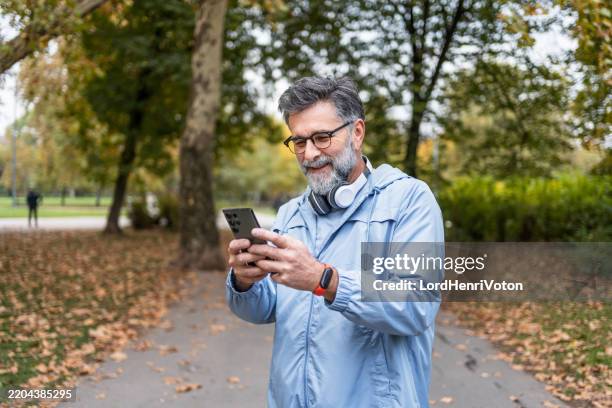 mature man using smartphone in the park - fitness tracker stock pictures, royalty-free photos & images