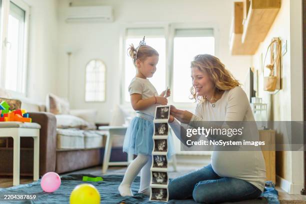expecting mother with daughter looking at ultrasound photos at home - sibling stock pictures, royalty-free photos & images