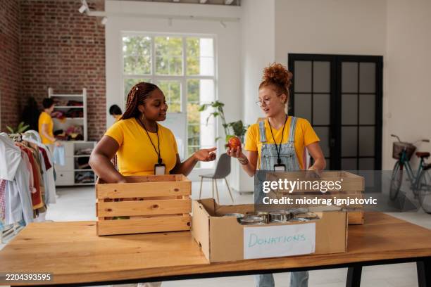 vielfältige junge frauen packen lebensmittel für wohltätige zwecke ein - chancengleichheit stock-fotos und bilder