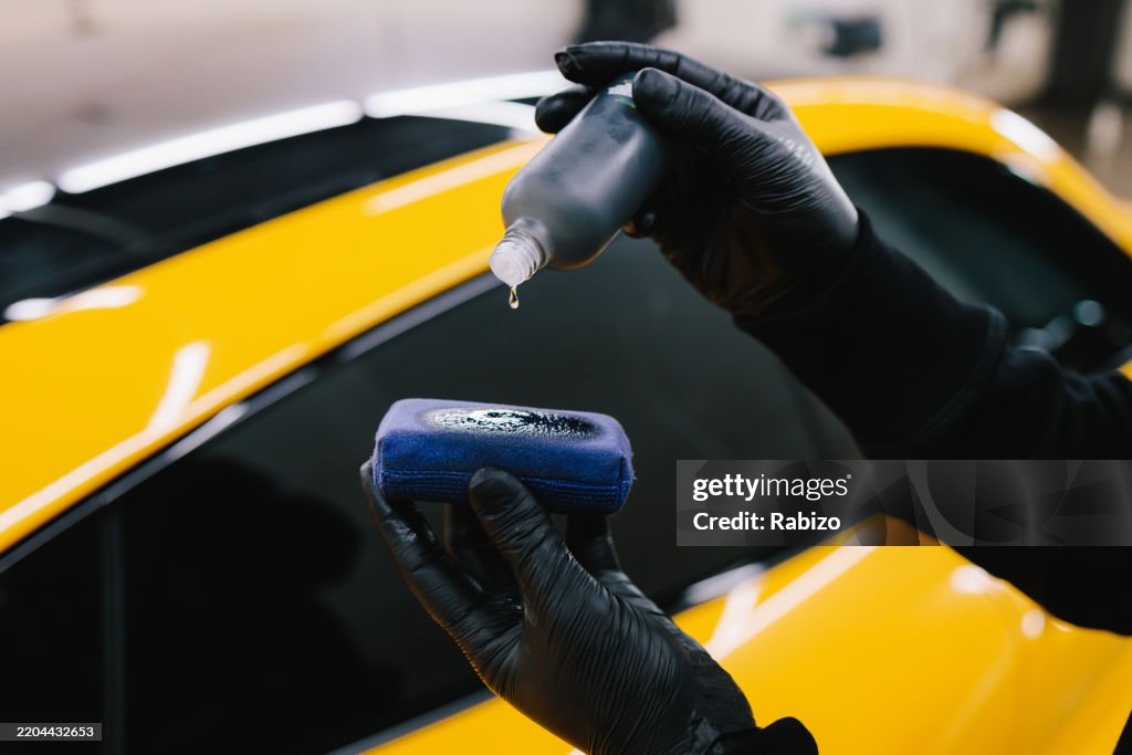Process of pouring ceramic liquid from bottle on sponge to apply a protective nano layer on car. Detailing service worker applies ceramic protective liquid on sponge close-up.