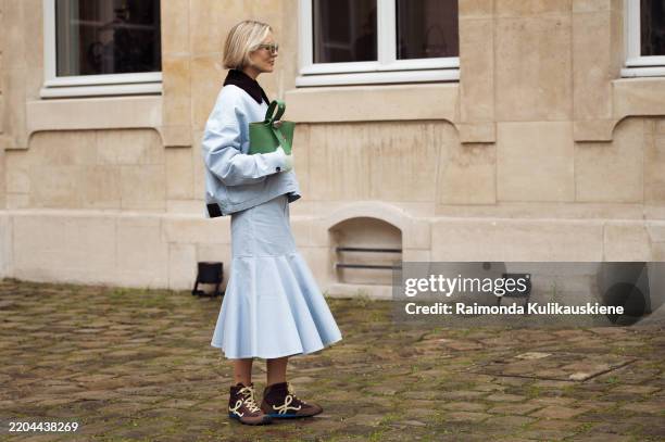 Violet Grace Atkinson wears light blue skirt, light blue jacket with black collar, green Loewe bag and brown and pale yellow sneakers outside the...
