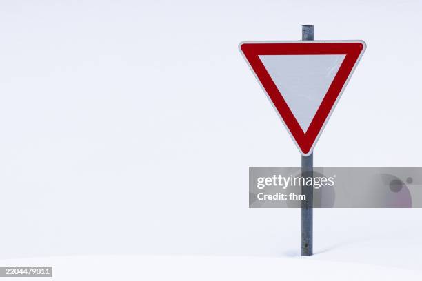 yield sign at a full snowcapped road - vorfahrt beachten stock-fotos und bilder