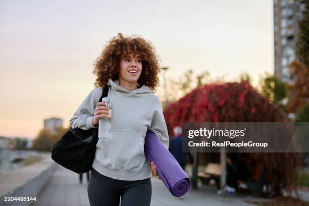 junge frau, die nach dem training mit yogamatte und sporttasche geht - sporttasche stock-fotos und bilder