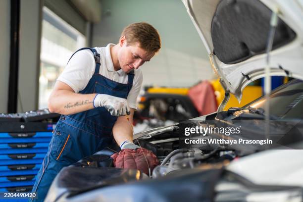 professional auto mechanic repairing vehicle engine in workshop setting - mécanicien automobile photos et images de collection