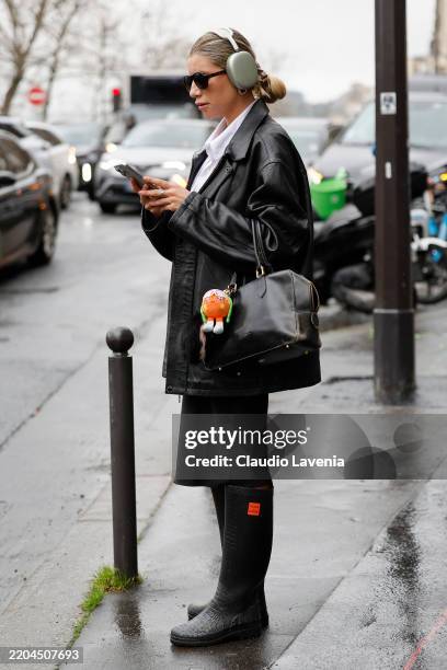Guest wears black leather jacket, black skirt, brown leather bag, black Aigle for Koché boots, outside Marine Serre, during the Womenswear...
