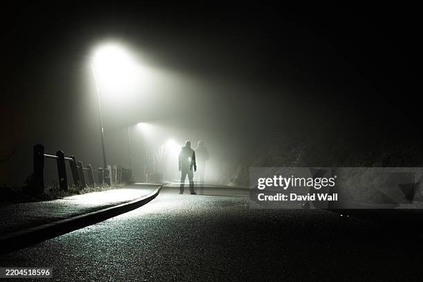 an eerie transparent ghost like figure standing on ampty road, silhouetted by street lights on a spooky foggy winters night - missing persons stock pictures, royalty-free photos & images