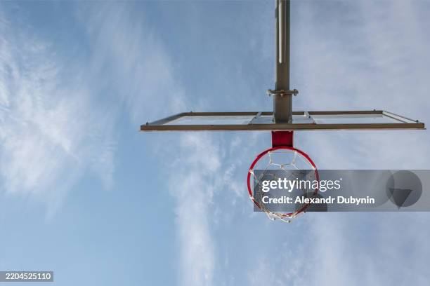 view from below basketball backboard with ring on basketball court against blue sky. concept basketball sport - scoreboard basketball stock pictures, royalty-free photos & images