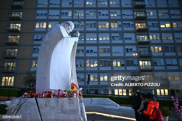 People pray at the statue of John Paul II outside the Gemelli hospital where Pope Francis is hospitalized with pneumonia, in Rome on March 14, 2025.