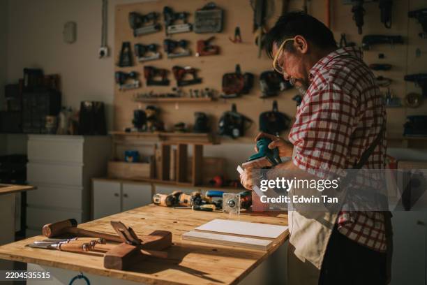 craftsmanship asian chinese senior carpenter using sander polishing piece of wood in woodshop - elektrisch gereedschap stockfoto's en -beelden