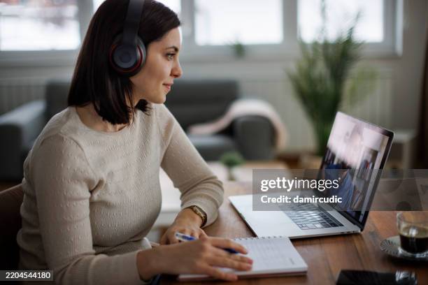 donna in cuffia che frequenta un corso online e prende appunti - videoconferenza foto e immagini stock