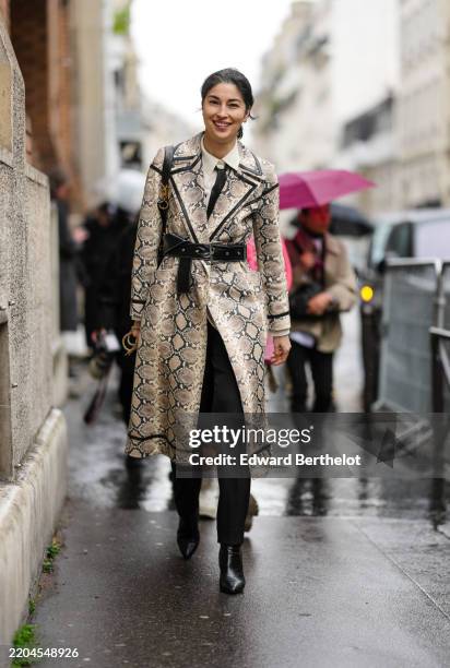 Caroline Issa wears white buttoned up long sleeve shirt, black necktie, light brown python snakeskin pattern/print belted trench leather coat, shiny...