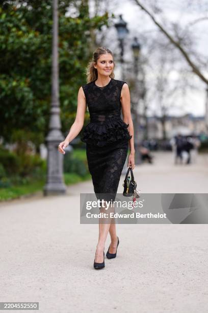 Guest wears black sheer mesh lace sleeveless ruffled midi dress, shiny black Miu Miu leather bag, floral bag charms, gold rings, white gold diamond...