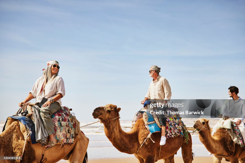 Medium wide shot family riding camels on beach in Morocco
