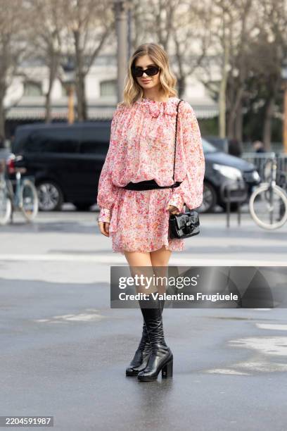 Xenia Adonts wears black sunglasses, a black leather cross-body Chanel bag, a black belt, black knee high leather heeled Chanel boots and a ruffles...