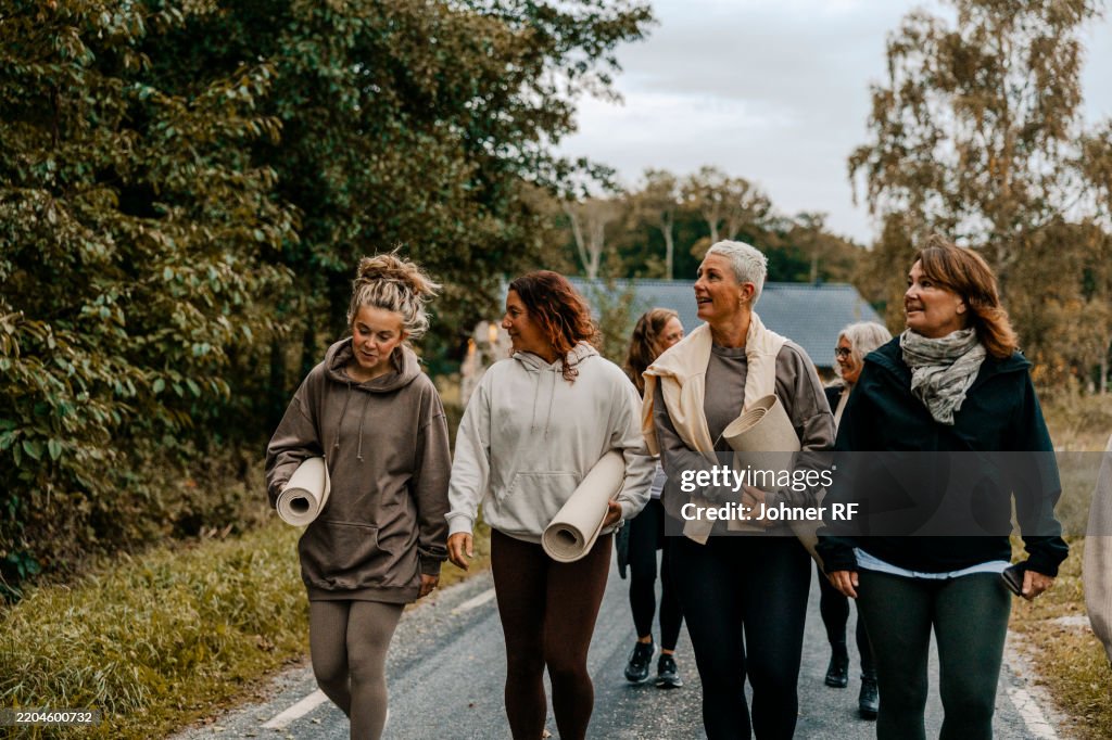 Group of female friends holding yoga mats and talking while going for class