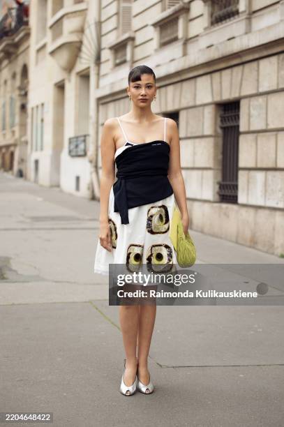 Guest wears a white and black printed Miu Miu midi dress, a Miu Miu leather grass green bag and silver open-toe pumps outside the Miu Miu fashion...