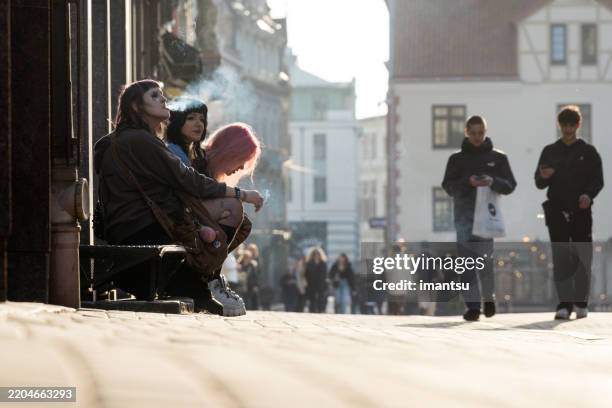 three young women sitting on the front door step of a building in old riga - riga latvia stock pictures, royalty-free photos & images