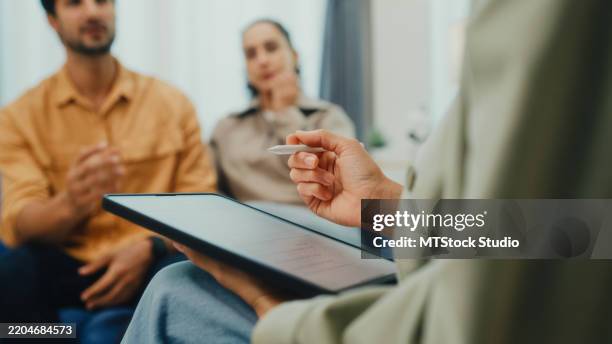 nahaufnahme eines jungen paares in ernsthafter diskussion mit einem psychiater während der eheberatungssitzung, die auf dem sofa im wohnzimmer zu hause sitzt. therapiesitzung konzept für psychische gesundheit. - eheberatung stock-fotos und bilder