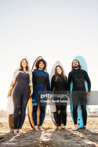 smiling surfers posing with their surfboards on the beach - neoprenanzug stock-fotos und bilder