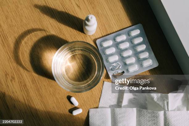 pills, nasal spray, tissues and glass of water illuminating by sunlight - cough medicine stock pictures, royalty-free photos & images