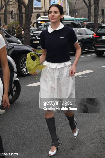 Guest wears a white Miu Miu polo, blue Miu Miu t-shirt, a white skirt, grey socks, silver heels and a yellow Miu Miu bag outside Miu Miu show during...