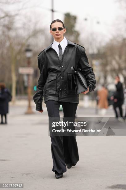 Guest wears black Chanel sunglasses, white buttoned up long sleeve shirt, shiny black woven leather necktie, shiny black oversized buttoned leather...