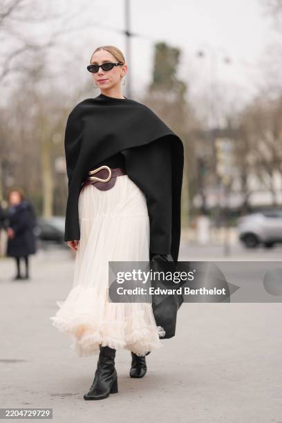 Guest wears black sunglasses, silver hoop earrings, black cape, shiny black silver detail leather belt, white sheer mesh tulle midi skirt, shiny...