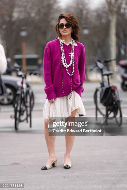 Guest wears white blazer jacket, shiny black quilted Chanel leather bag, navy blue white pearl pattern/print Chanel denim jean pants, gold rings,...