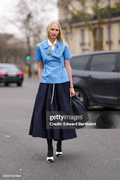 Guest wears white collar buttoned up Miu Miu shirt, light blue Miu Miu shirt, silver floral Miu Miu brooch, navy blue Miu Miu midi skirt, shiny dark...