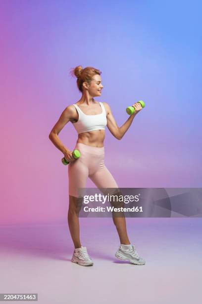 smiling woman exercising with dumbbells against colored background - dumbbell stock pictures, royalty-free photos & images