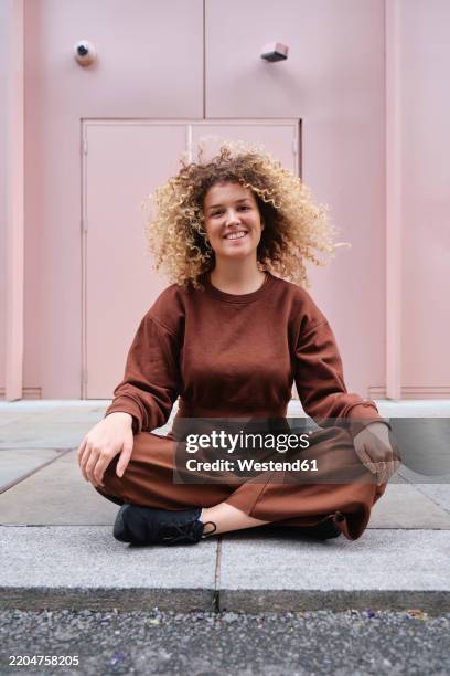 smiling woman sitting cross-legged on sidewalk - hand on knee stock pictures, royalty-free photos & images