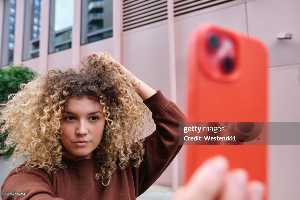 Woman with hand in hair taking selfie through smart phone