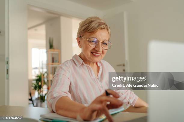 senior woman studying online and taking notes - boomer computer stock pictures, royalty-free photos & images