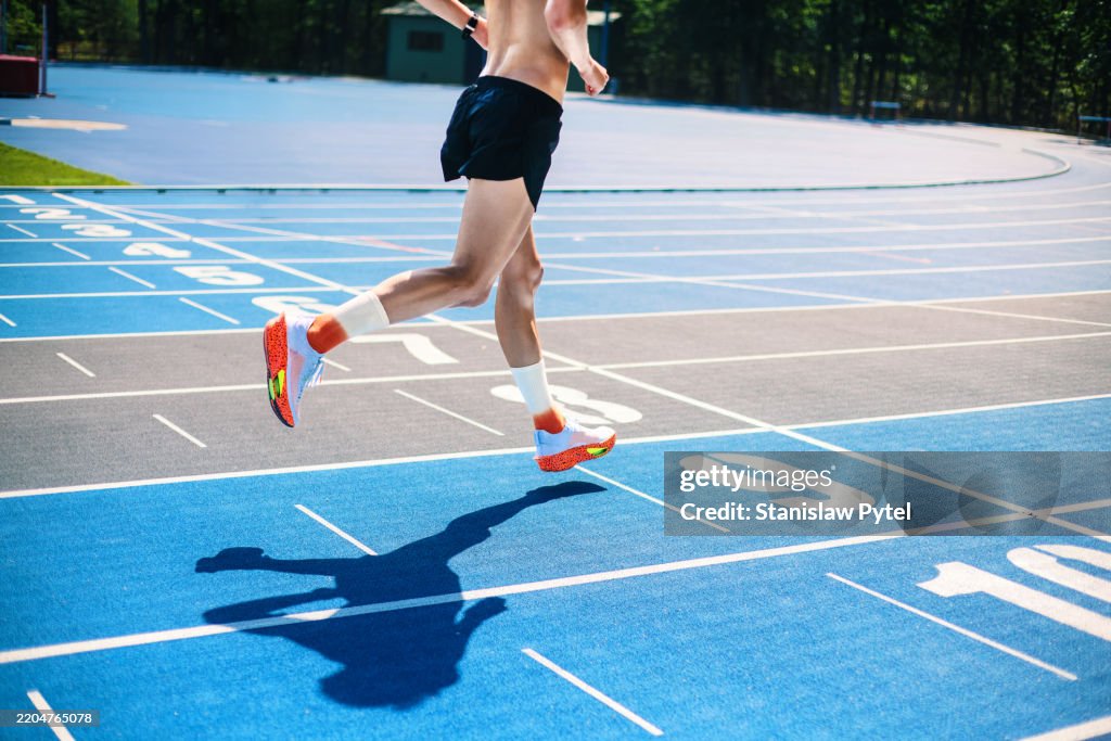 View on athlete's legs running on blue stadium on sunny day
