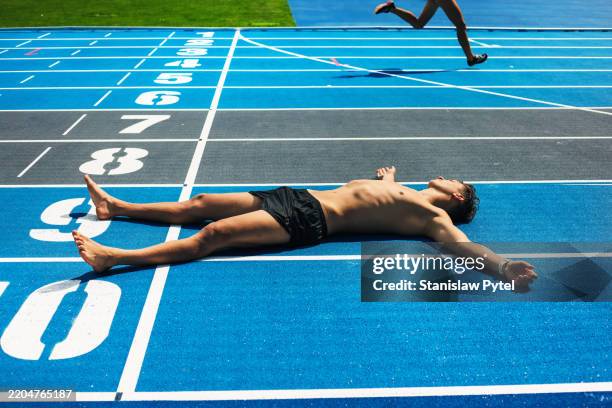 pentathletee lying on blue stadium after taking ice bath and laser run team training for international level competition, sunny day, another athelete running in background - scalzo foto e immagini stock