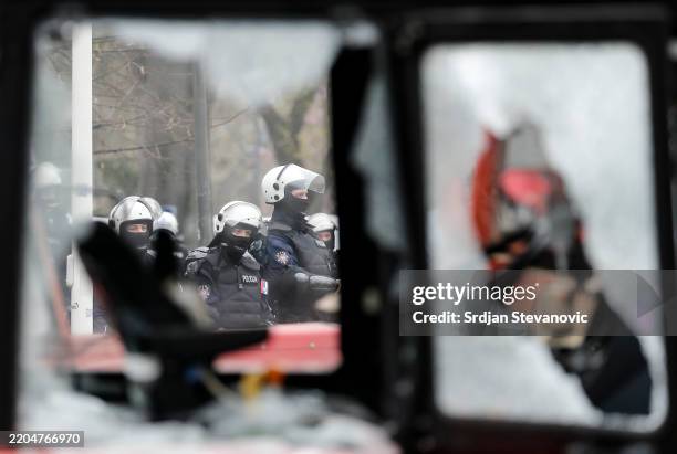 Police officers stand guard, pictured through a broken window of a tractor, during the student-led rally on March 15, 2025 in Belgrade, Serbia. In...