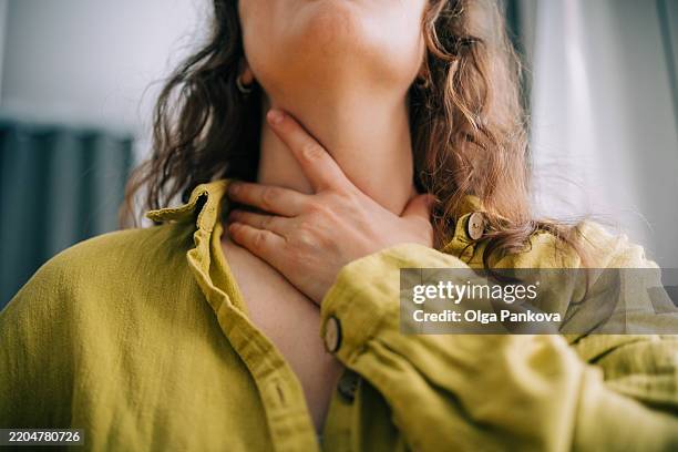 woman suffering from sore throat holding her neck - kehle stock-fotos und bilder