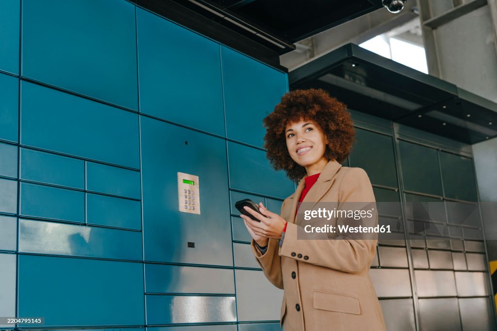 Smiling businesswoman using smartphone near locker at parking lot
