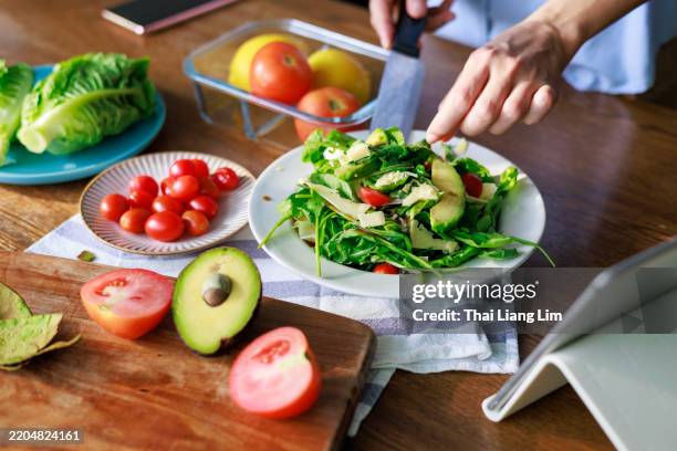 préparation saine d’une salade d’avocats et de tomates à l’aide d’une tablette numérique pour vous guider. - roquette photos et images de collection