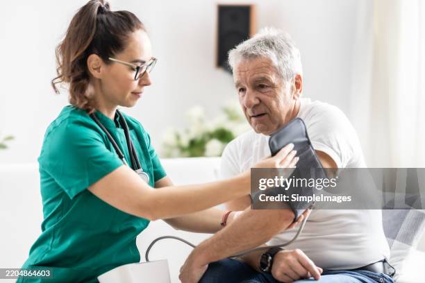 female doctor measuring senior patient’s blood pressure at home - messinstrument stock-fotos und bilder
