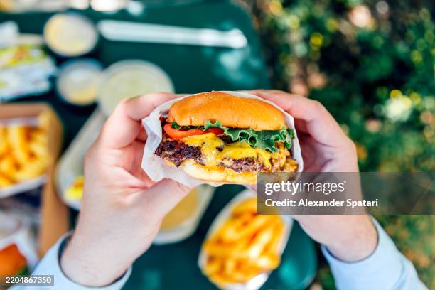 man eating juicy cheeseburger, personal perspective view - schnellimbiss stock-fotos und bilder
