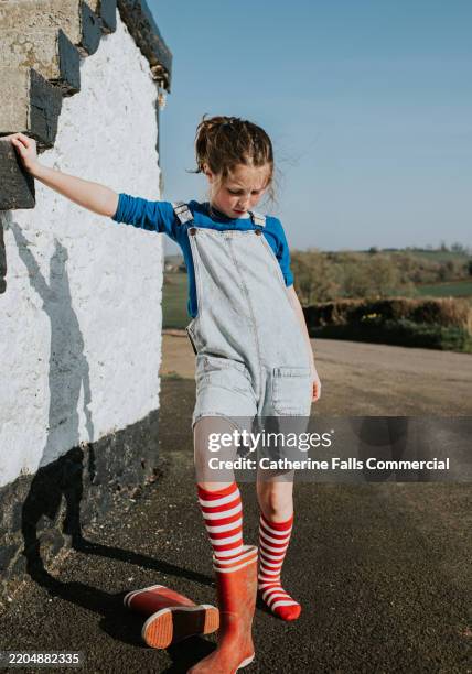 a little girl puts on a pair of waterproof red wellington boots on a sunny day - hot small girl stock pictures, royalty-free photos & images