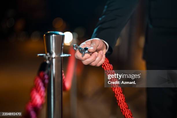 close-up of male security guard holding red rope barrier at night - rope barrier stock pictures, royalty-free photos & images