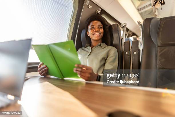 businesswoman smiling while working on a train journey with documents - elektrische trein stockfoto's en -beelden