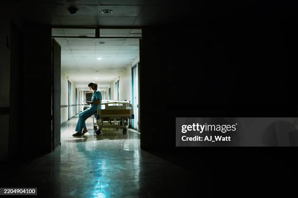 professional nurse in scrubs using mobile phone leaning on gurney at night - working overtime stock pictures, royalty-free photos & images
