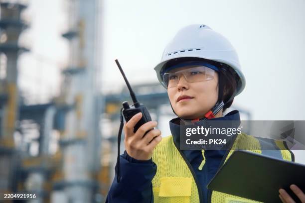 asian female engineers are working on digital tablet in a petrochemical plant. - china chemical industry stock pictures, royalty-free photos & images