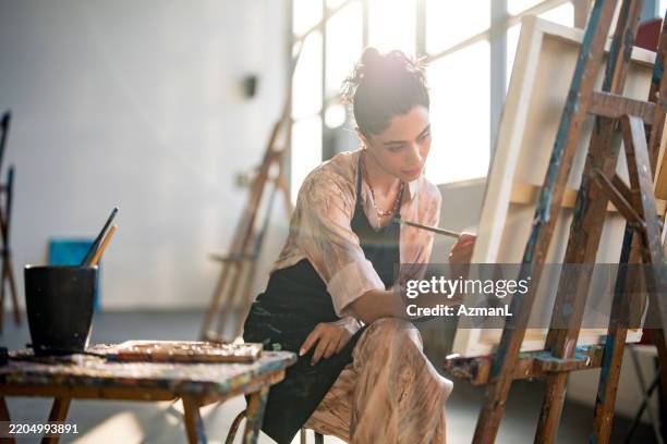 young middle eastern artist creating artwork in sun-drenched studio with wooden easel - kunstatelier stockfoto's en -beelden