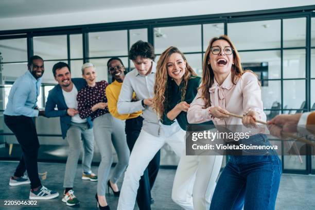 playful colleagues having fun while playing tug-of-war in the office. - tug of war stock pictures, royalty-free photos & images