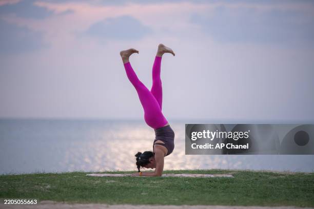 la donna pratica yoga all'aperto vicino all'oceano durante il crepuscolo, in equilibrio in un grazioso piegamento all'indietro. - piegarsi allindietro foto e immagini stock