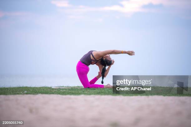 la donna pratica yoga all'aperto vicino all'oceano durante il crepuscolo, in equilibrio in un grazioso piegamento all'indietro. - piegarsi allindietro foto e immagini stock